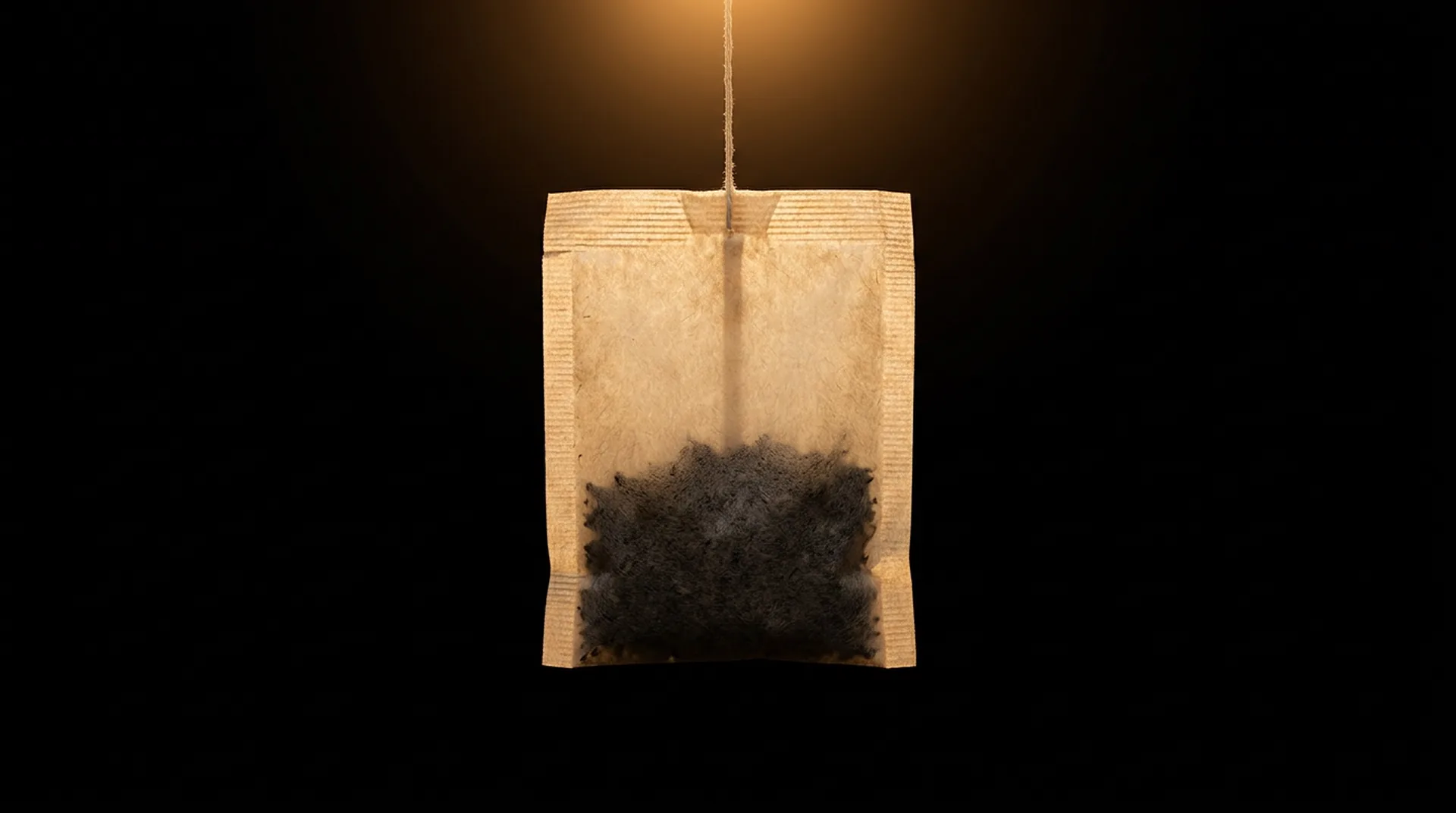 A closed paper tea bag hanging in the dark