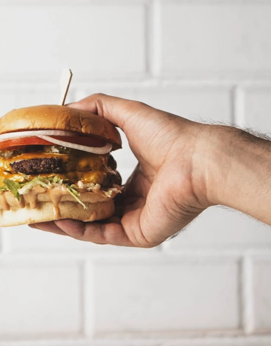 A hand holding a cheeseburger against a white wall